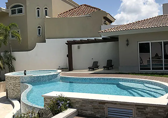Alberca residencial con jacuzzi elevado y muros de piedra